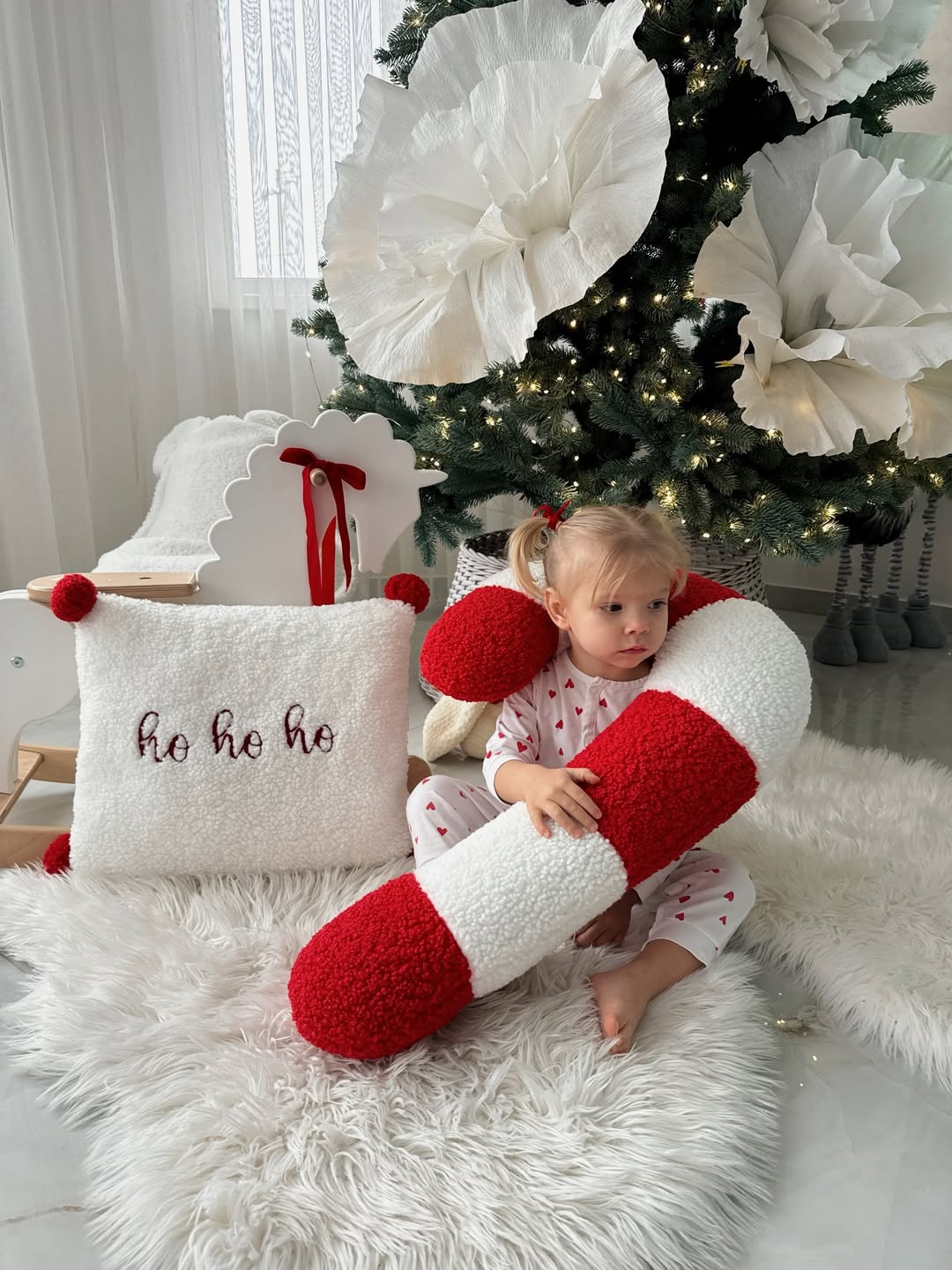 Bambina sul tappeto con cuscino bastoncino di zucchero e cuscino ho ho ho in bouclé davanti all'albero di Natale.