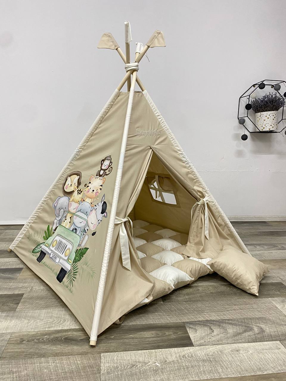 Tenda da gioco a forma di teepee per bambini, tessuto beige con illustrazioni dipinte a mano di animali della savana come leoni, elefanti, giraffe e zebre; apertura frontale a forma di arco, pavimento morbido interno, personalizzabile con il nome del bambino, ideale per playroom o cameretta a tema safari.