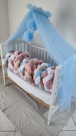 Varianti di paracolpi a treccia per lettino in diverse sfumature di rosa, azzurro e beige sotto un baldacchino in tulle.