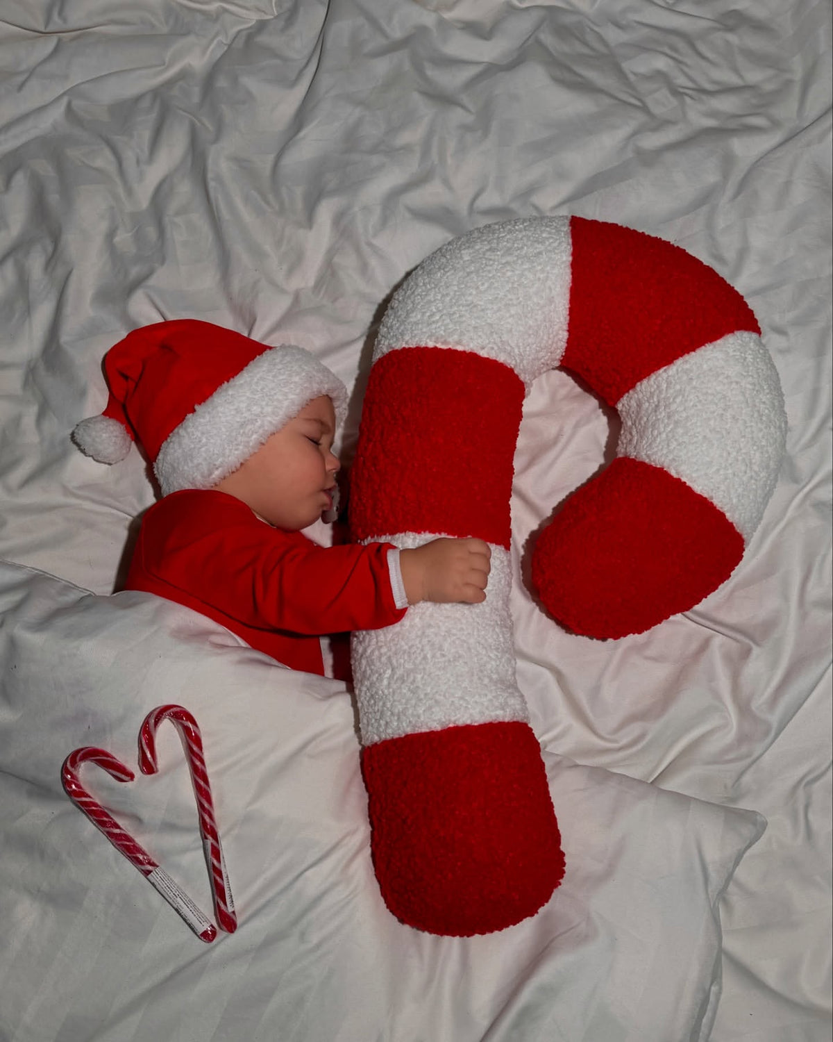Cuscino natalizio candy cane in bouclé morbido accanto a un neonato addormentato con cappello di Babbo Natale