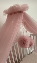 Baldacchino in tulle rosa per lettino con pompon decorativi appesi