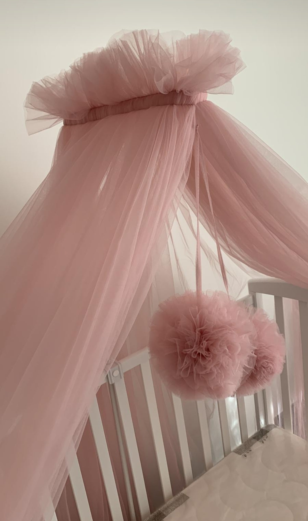 Baldacchino in tulle rosa per lettino con pompon decorativi appesi