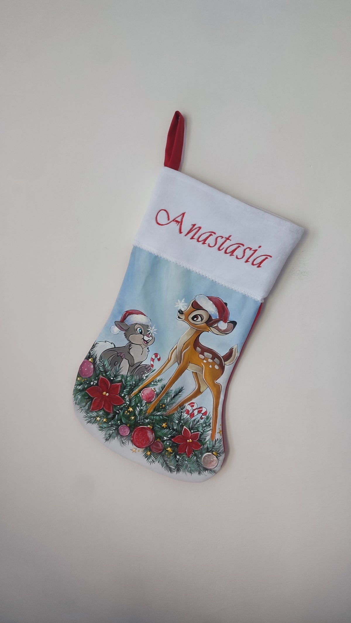 Calza di Natale azzurra dipinta a mano con illustrazione di Bambi e il coniglietto Tamburino tra rami di pino e sfere rosse.