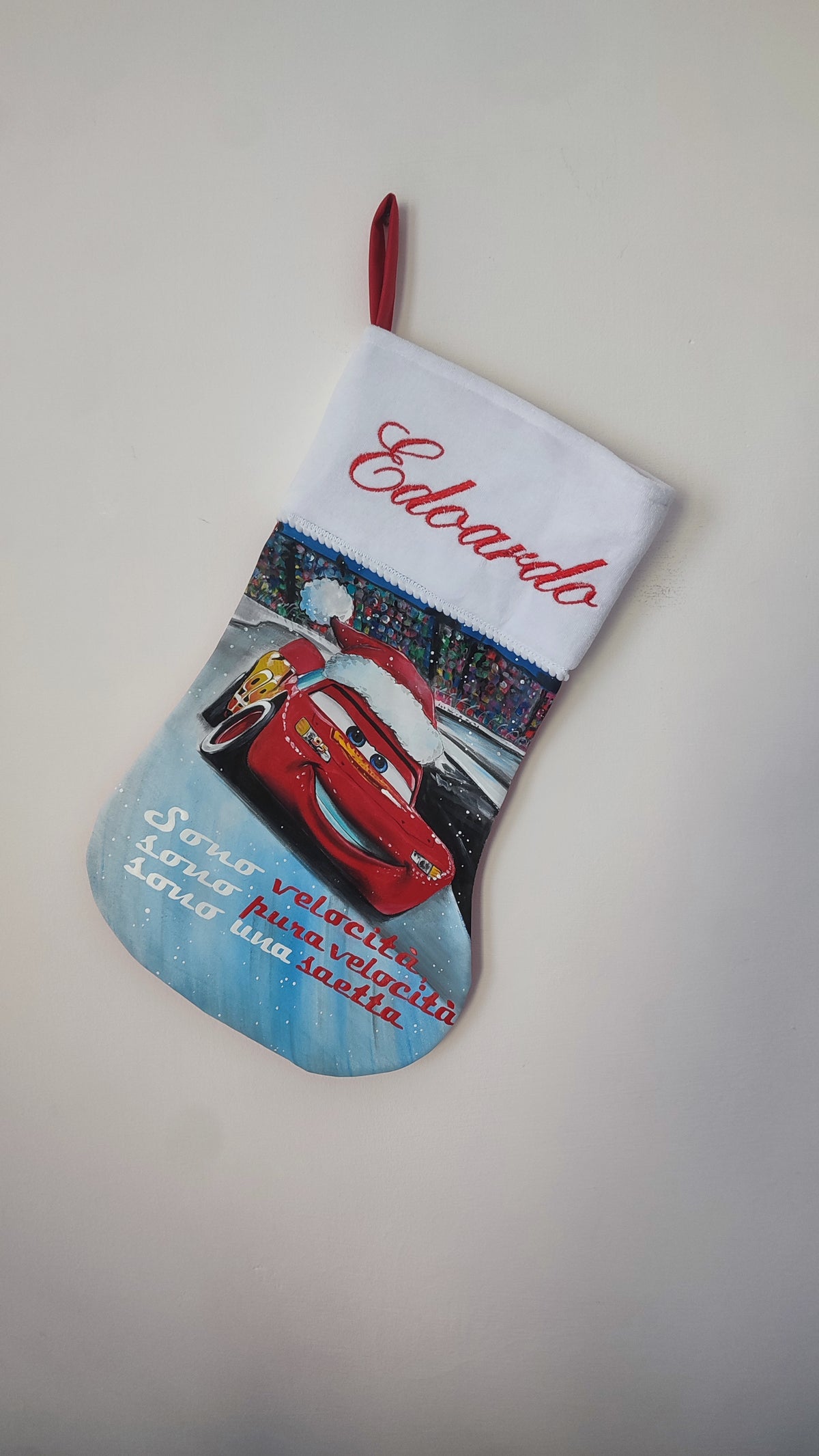 Calza di Natale azzurra dipinta a mano con illustrazione di Saetta McQueen con cappello natalizio e la scritta sono velocità.