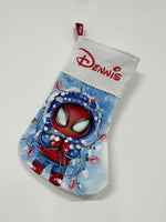 Calza di Natale azzurra dipinta a mano con illustrazione di Spiderman con cappuccio, avvolto da fili di luci natalizie.