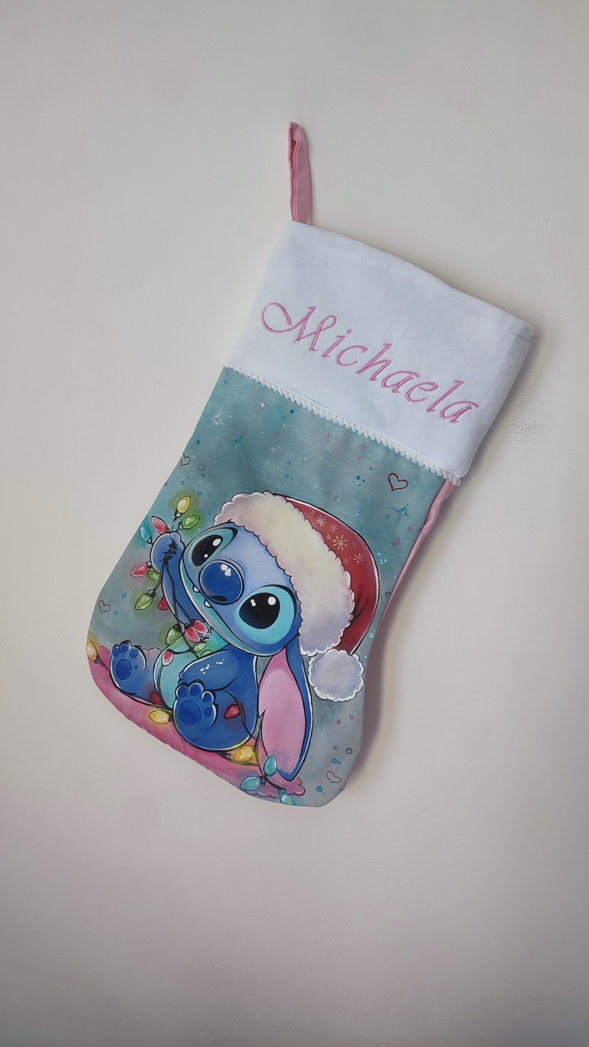 Calza di Natale azzurra dipinta a mano con illustrazione di Stitch con cappello di Babbo Natale, luci colorate e cuoricini.