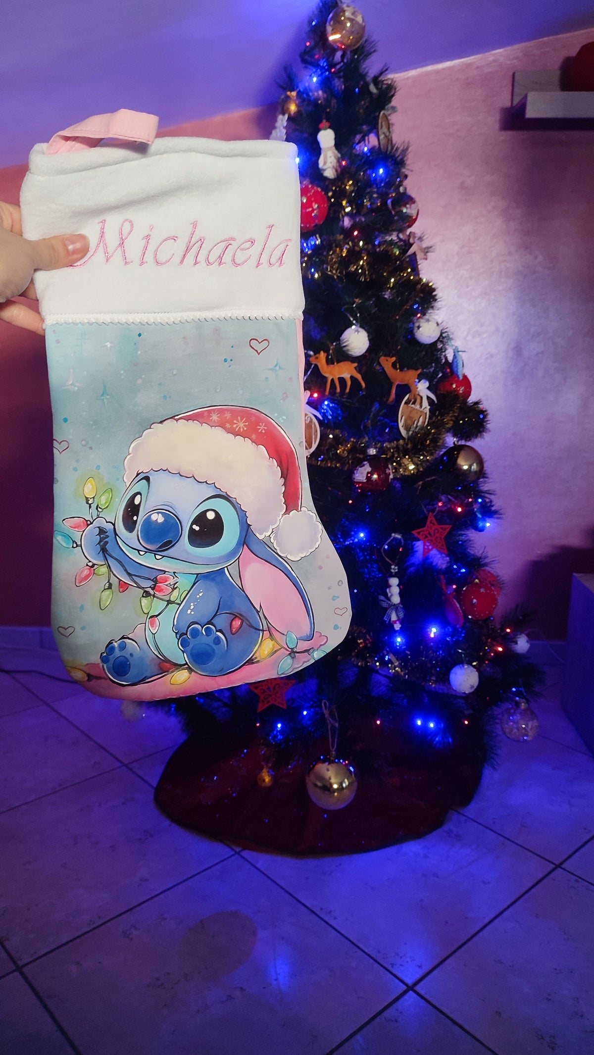 Calza di Natale azzurra dipinta a mano con illustrazione di Stitch con cappello di Babbo Natale, luci colorate e cuoricini.