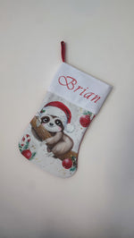 Calza di Natale bianca dipinta a mano con illustrazione di un bradipo con cappello di Babbo Natale, sfere rosse e stelline.