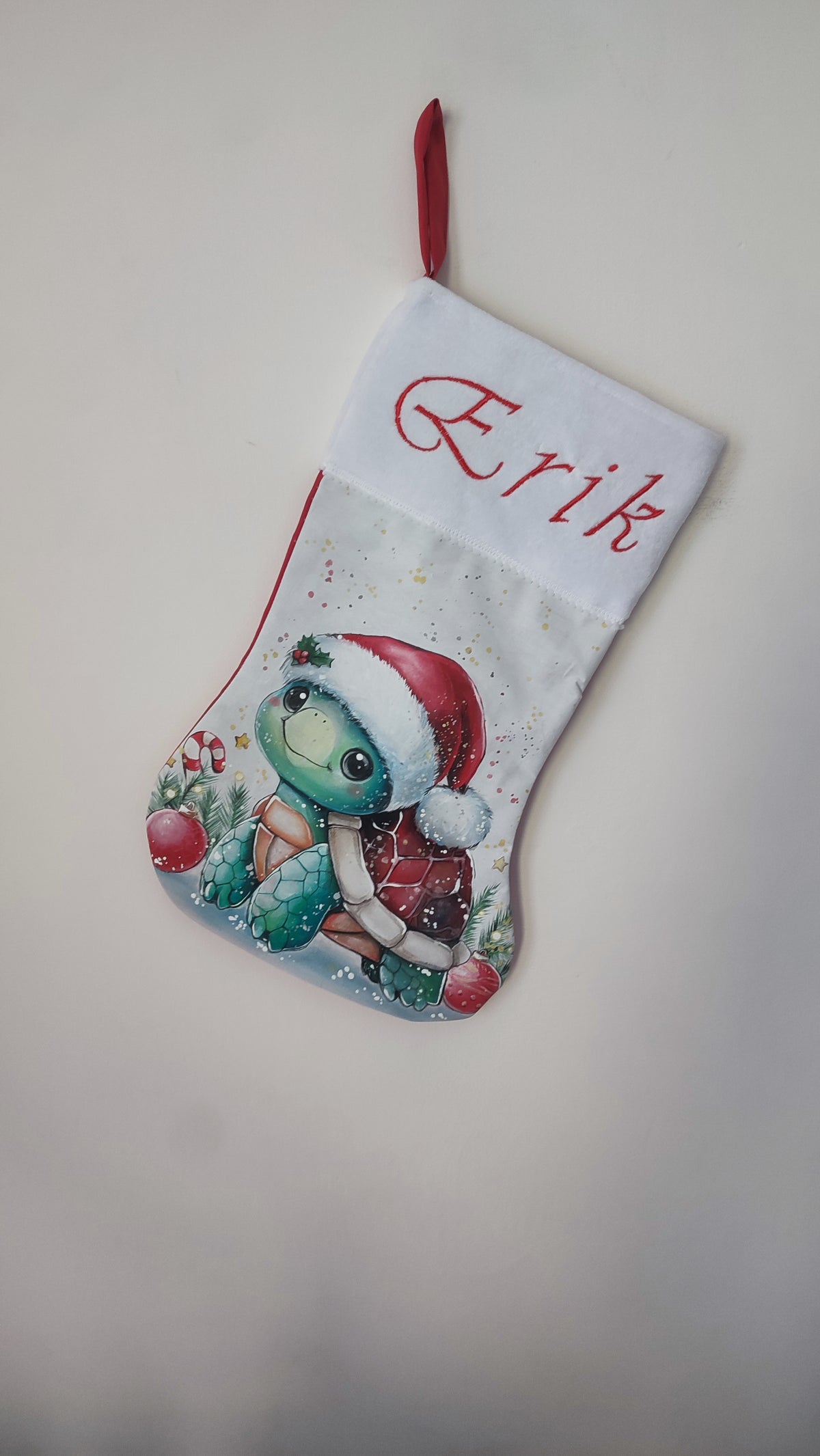 Calza di Natale bianca dipinta a mano con illustrazione di una tartaruga con cappello di Babbo Natale e bastoncini di zucchero.