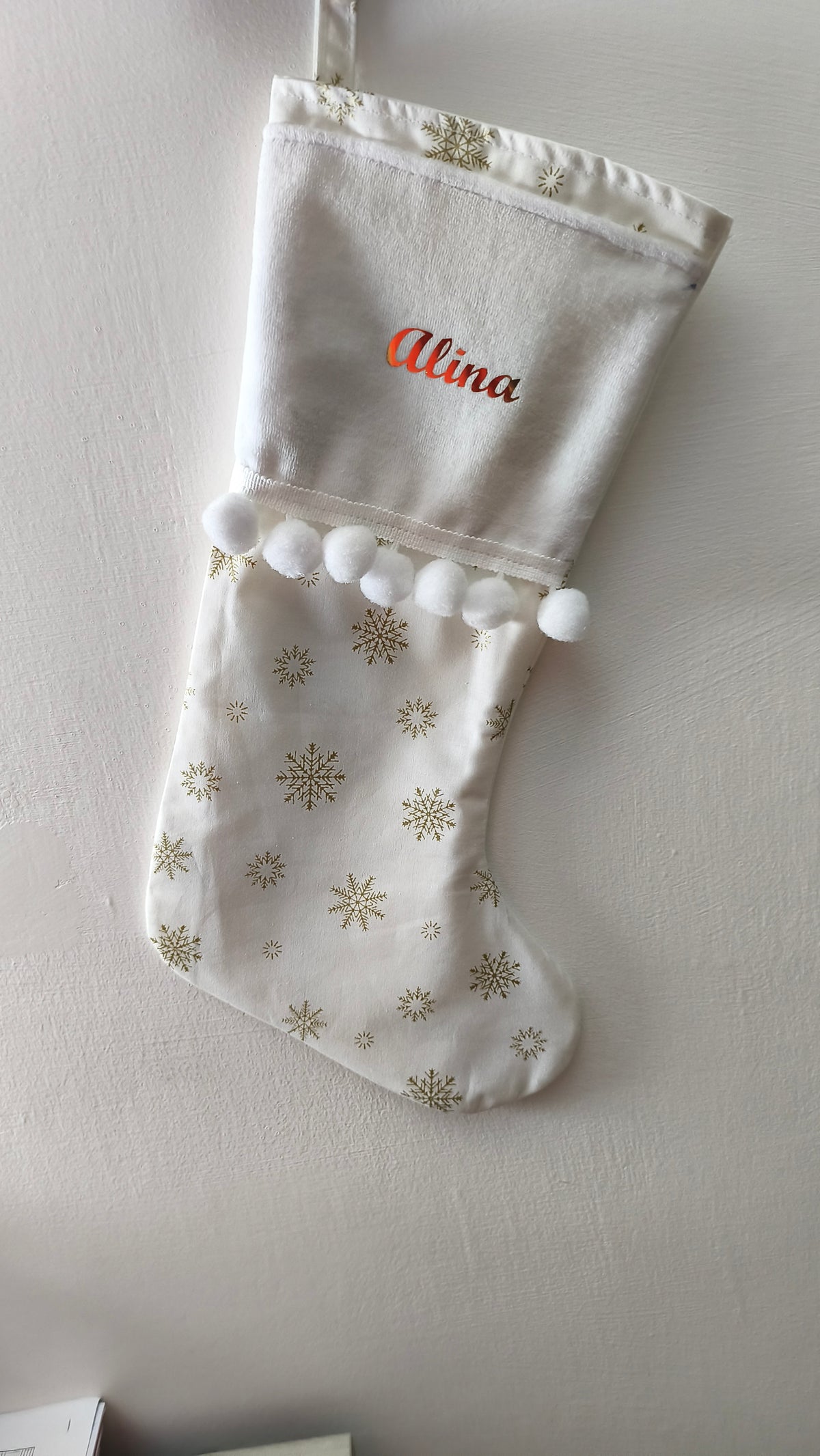 Calza di Natale avorio personalizzata con nome ricamato in rosso, delicati fiocchi di neve dorati e linea di pom pom bianchi.