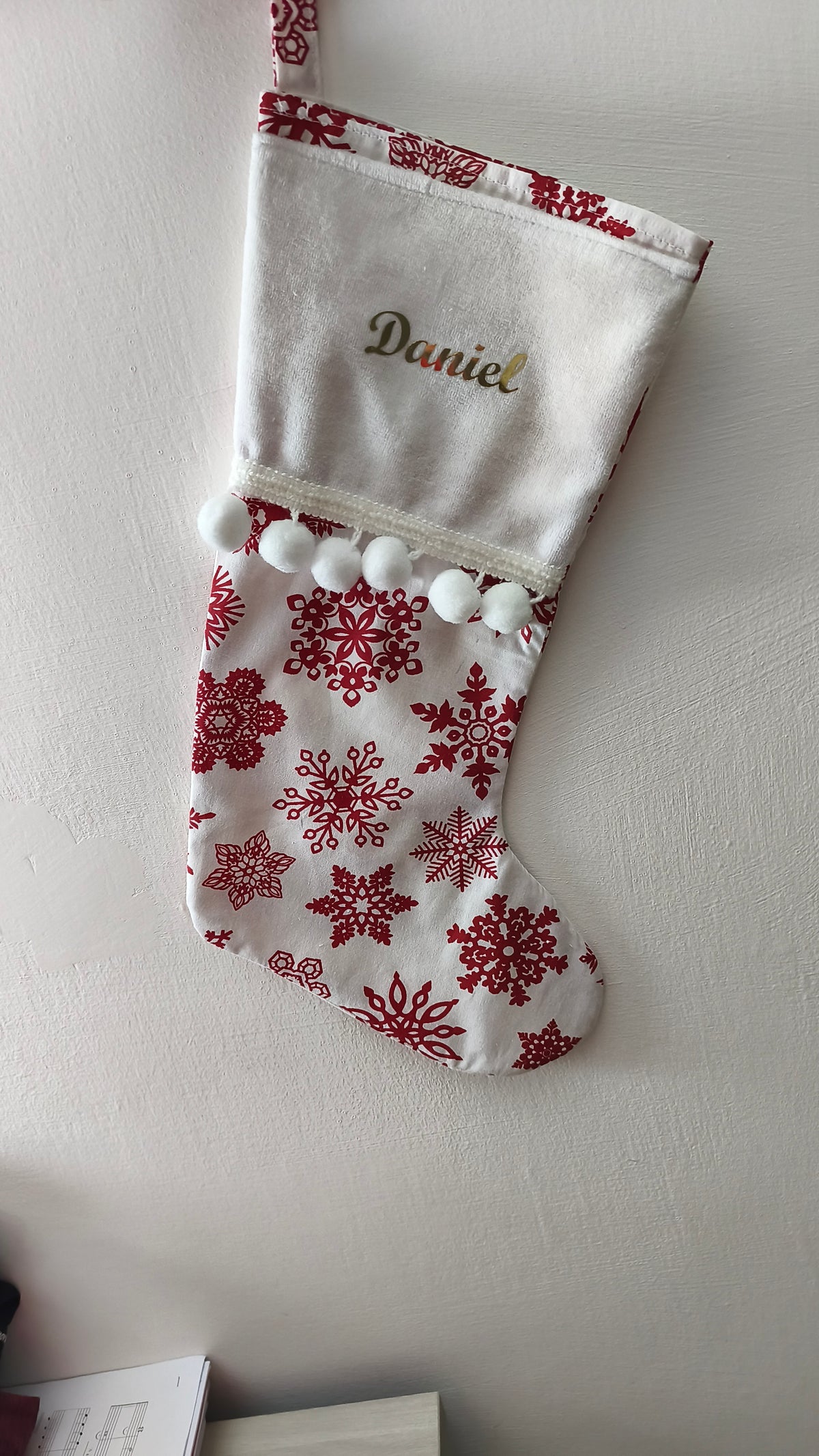 Calza di Natale bianca personalizzata con nome ricamato in filo oro, motivo di fiocchi di neve rossi e pom pom bianchi morbidi.
