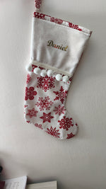 Calza di Natale bianca personalizzata con nome ricamato in filo oro, motivo di fiocchi di neve rossi e pom pom bianchi morbidi.