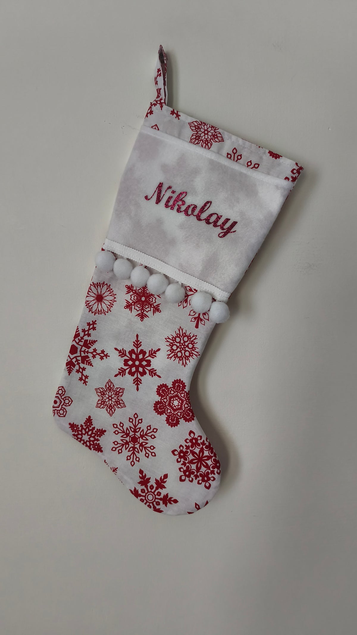 Calza di Natale bianca e rossa personalizzata con nome ricamato, grandi fiocchi di neve rossi e fila di pom pom bianchi.