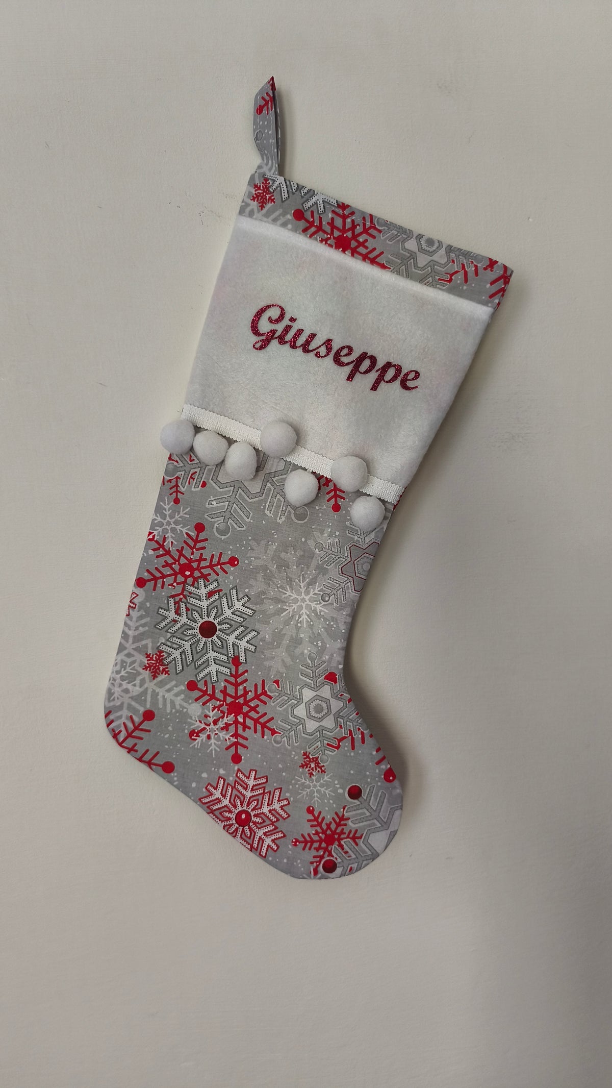 Calza di Natale grigia personalizzata con nome ricamato in rosso, motivi di fiocchi di neve rossi e argento con pom pom bianchi.