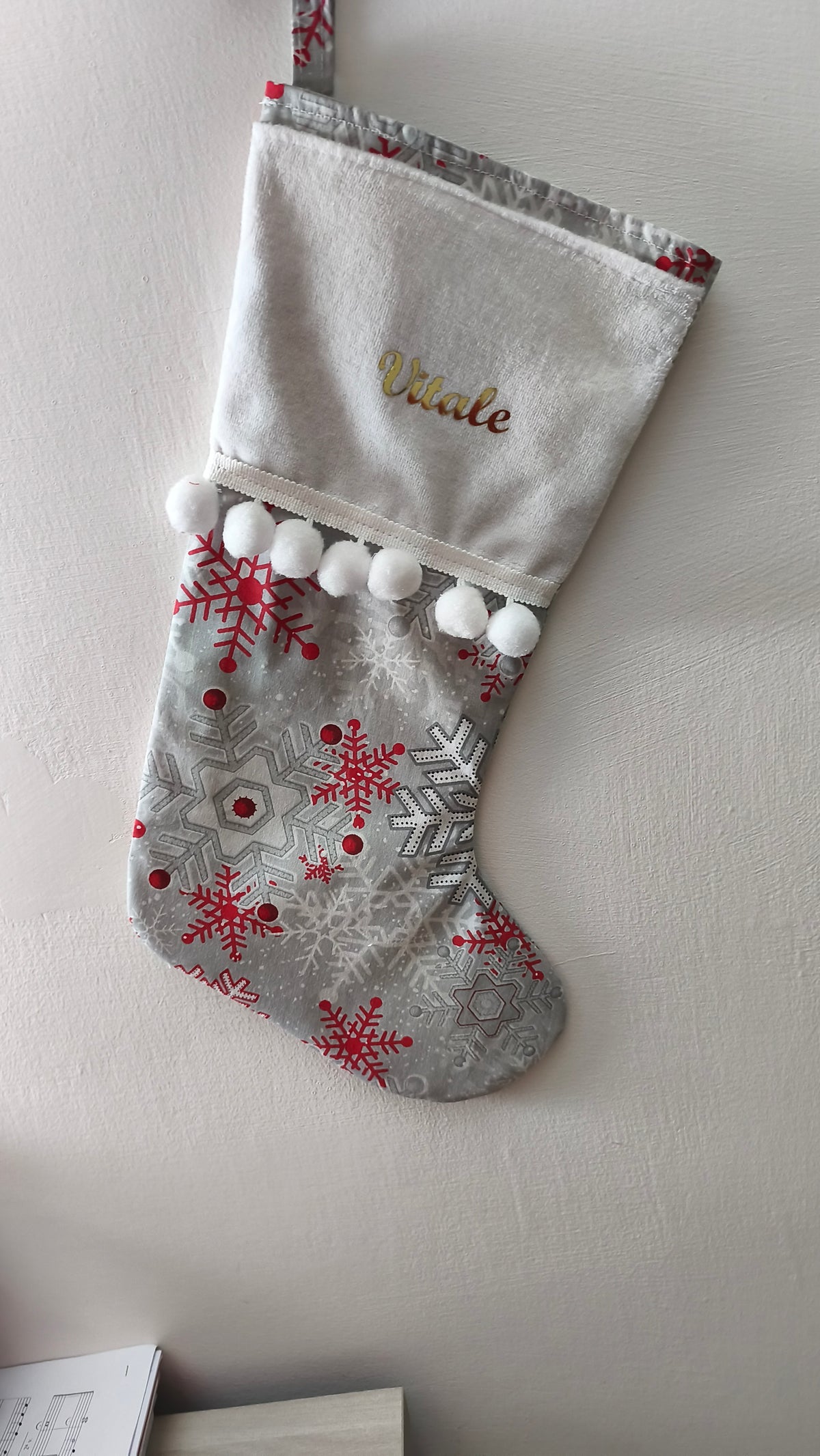 Calza di Natale grigia personalizzata con nome ricamato in oro, stampe di fiocchi di neve rossi e argento con pom pom bianchi.