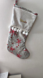 Calza di Natale grigia personalizzata con nome ricamato in oro, stampe di fiocchi di neve rossi e argento con pom pom bianchi.