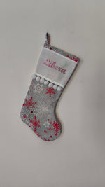Calza di Natale grigia personalizzata con nome ricamato in filo rosa glitter, stampe di fiocchi di neve rossi e pom pom bianchi.