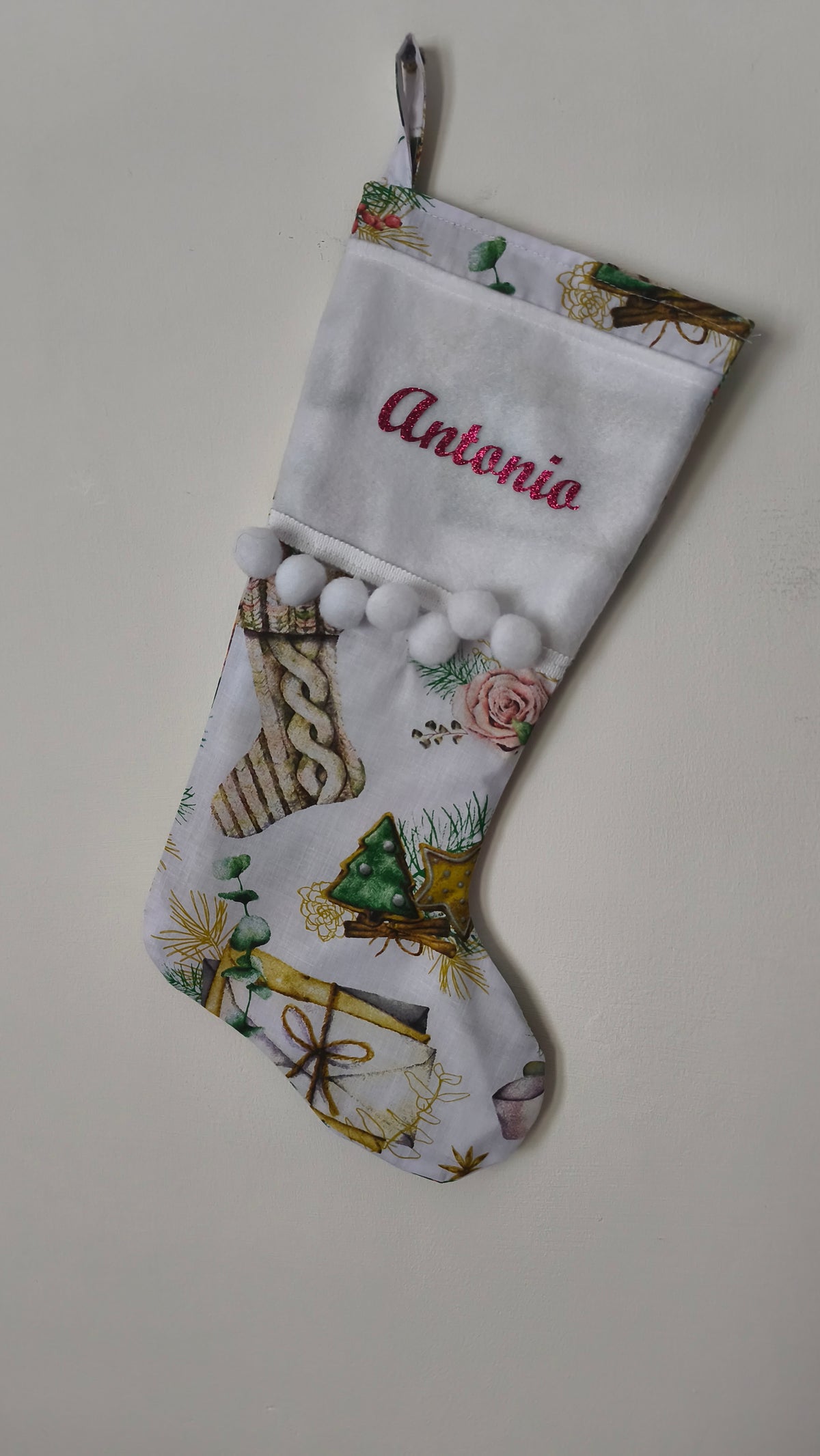 Calza di Natale bianca personalizzata con nome ricamato, illustrazioni di alberi di Natale, pacchi regalo e pom pom bianchi.