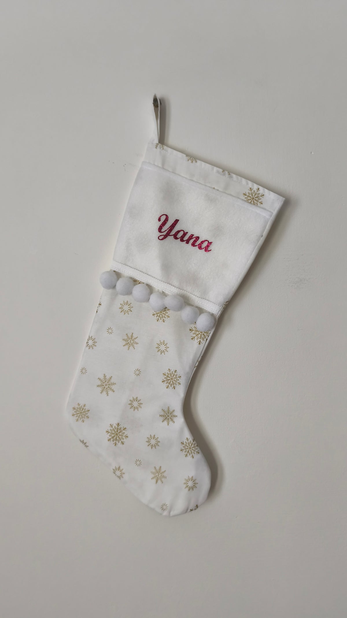 Calza di Natale bianca personalizzata con il nome Yana ricamato in rosso, stampe di fiocchi di neve oro e pom pom bianchi.