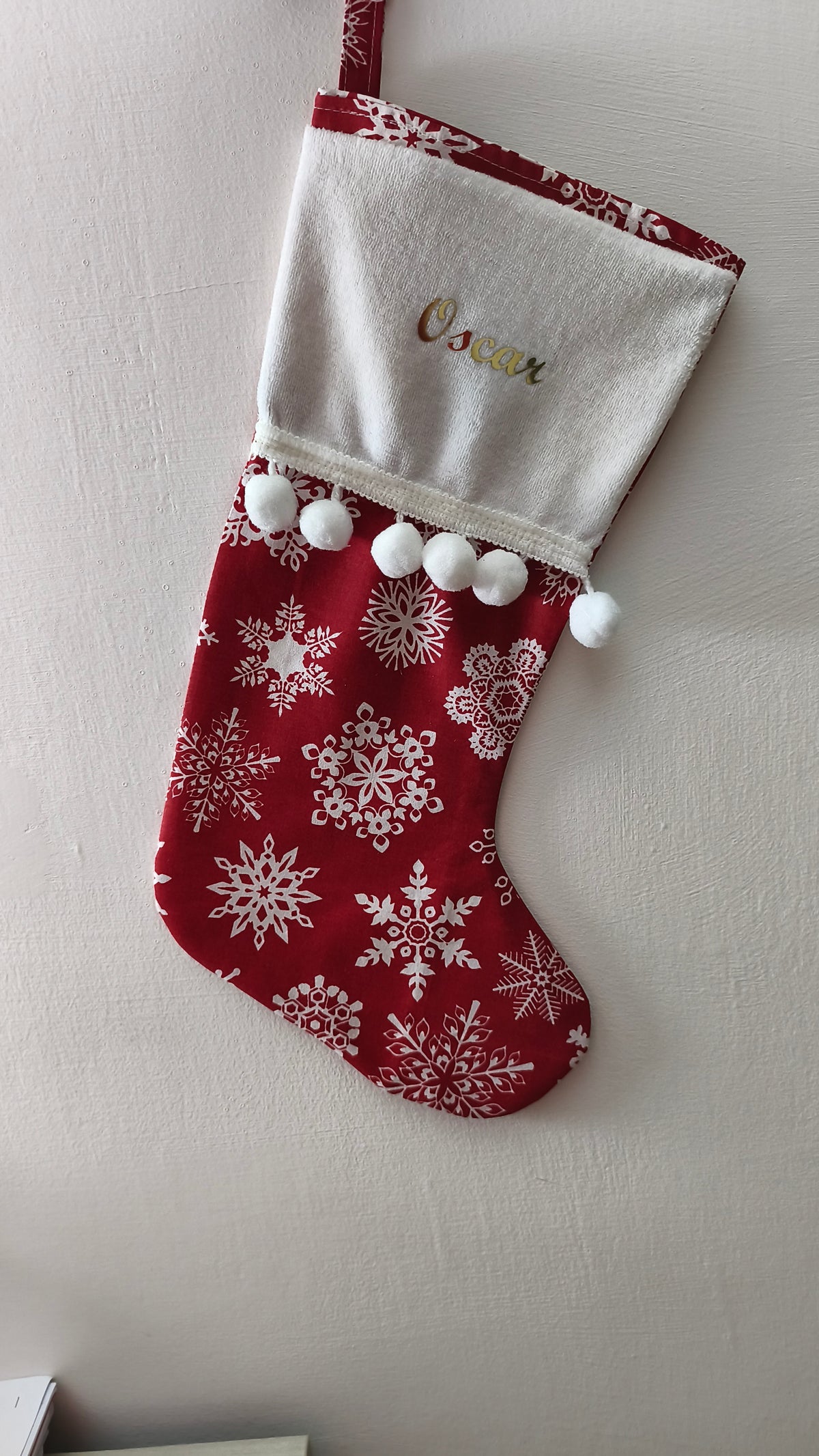 Calza di Natale rossa personalizzata con nome ricamato in oro, motivo di fiocchi di neve bianchi e pom pom bianchi morbidi.