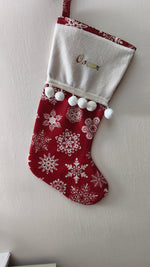 Calza di Natale rossa personalizzata con nome ricamato in oro, motivo di fiocchi di neve bianchi e pom pom bianchi morbidi.