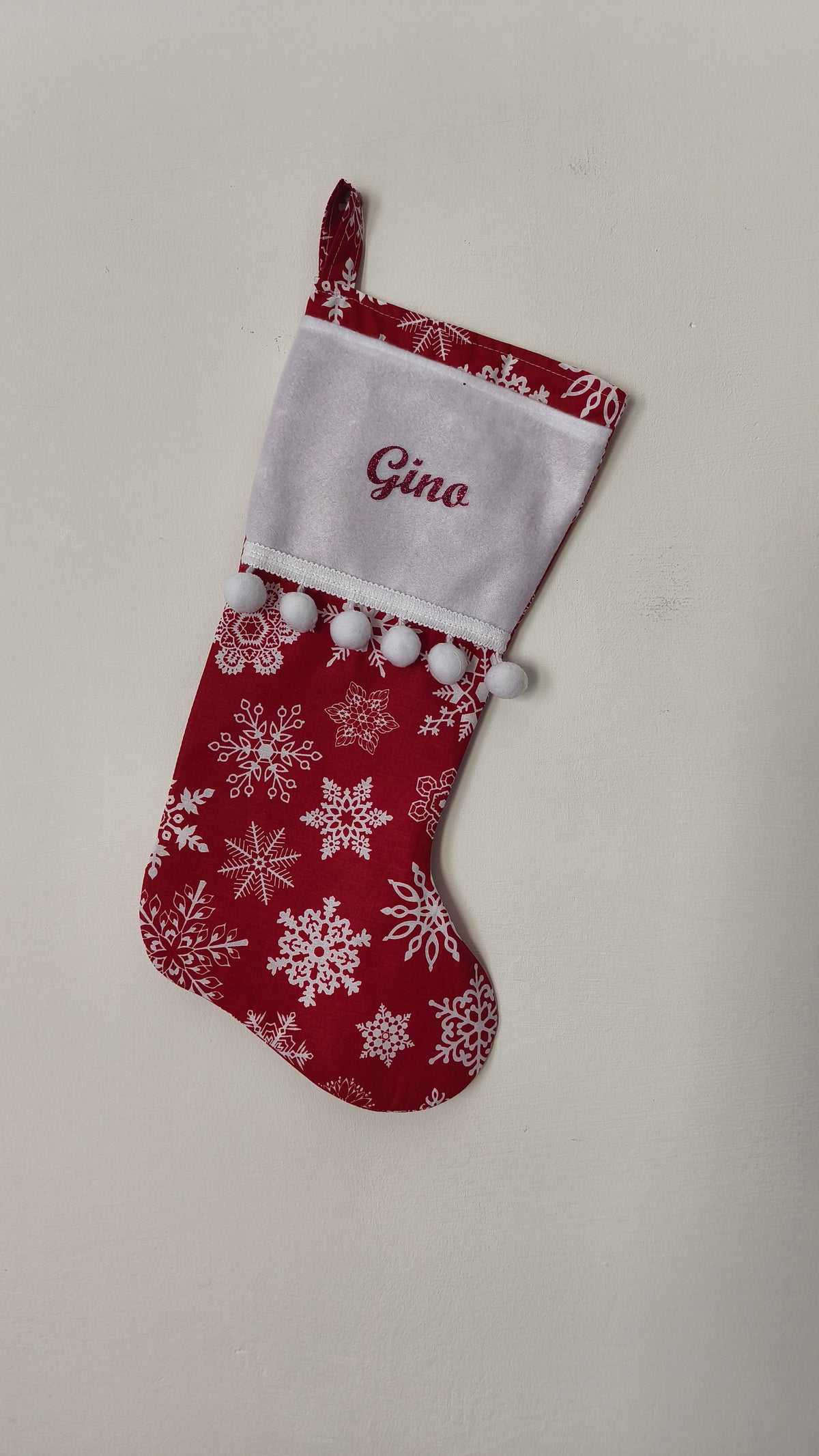 Calza di Natale rossa personalizzata con nome ricamato in rosso, motivo di fiocchi di neve bianchi e pom pom bianchi morbidi