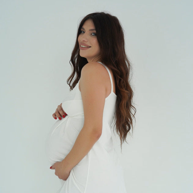 Donna in gravidanza di profilo indossa camicia da notte premaman bianca, morbida e comoda sul pancione