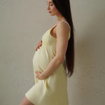 Donna in gravidanza di profilo indossa camicia da notte premaman giallo pastello con spalline sottili, morbida sul pancione