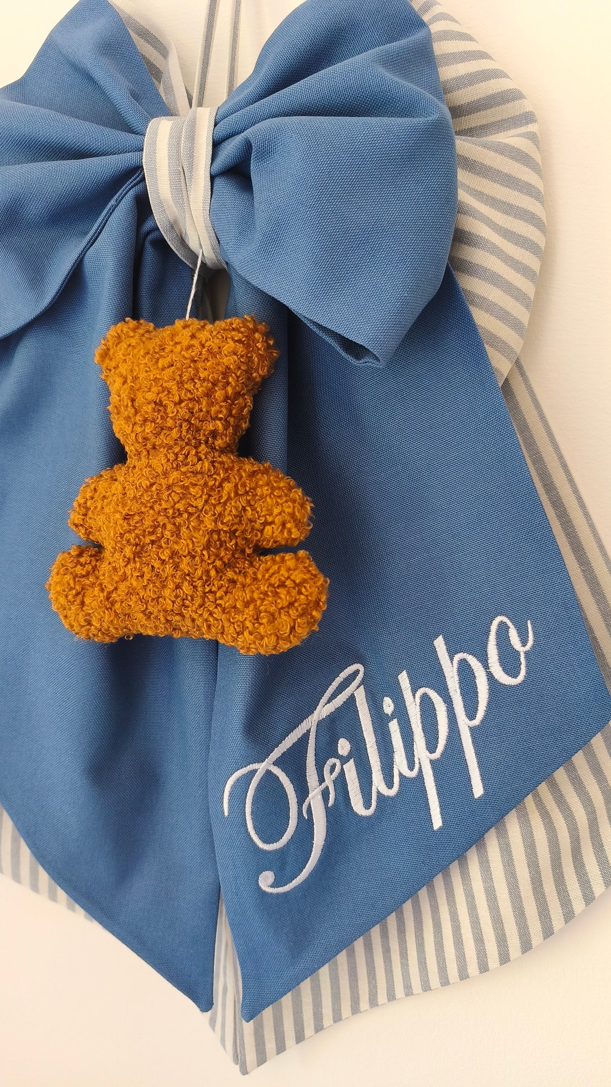 Coccarda nascita azzurro blu con bordo righe grigie, orsetto peluche color miele e scritta nome