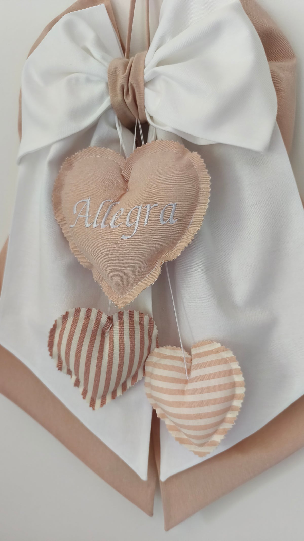 Primo piano coccarda nascita con cuore in tessuto e nome ricamato, tema beige