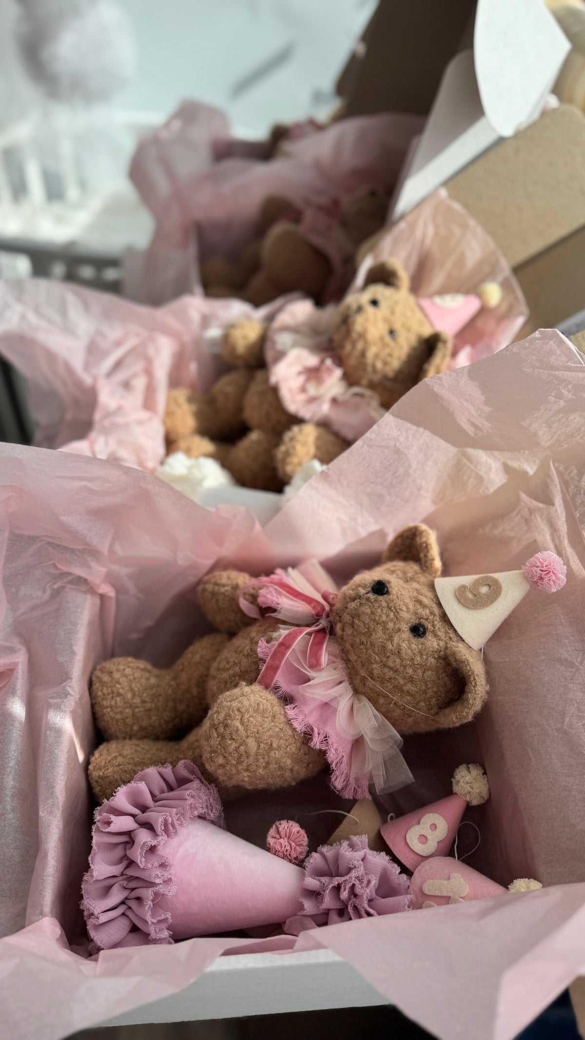 Scatole regalo aperte con orsetti di peluche e cappellini numerati rosa per la crescita del neonato