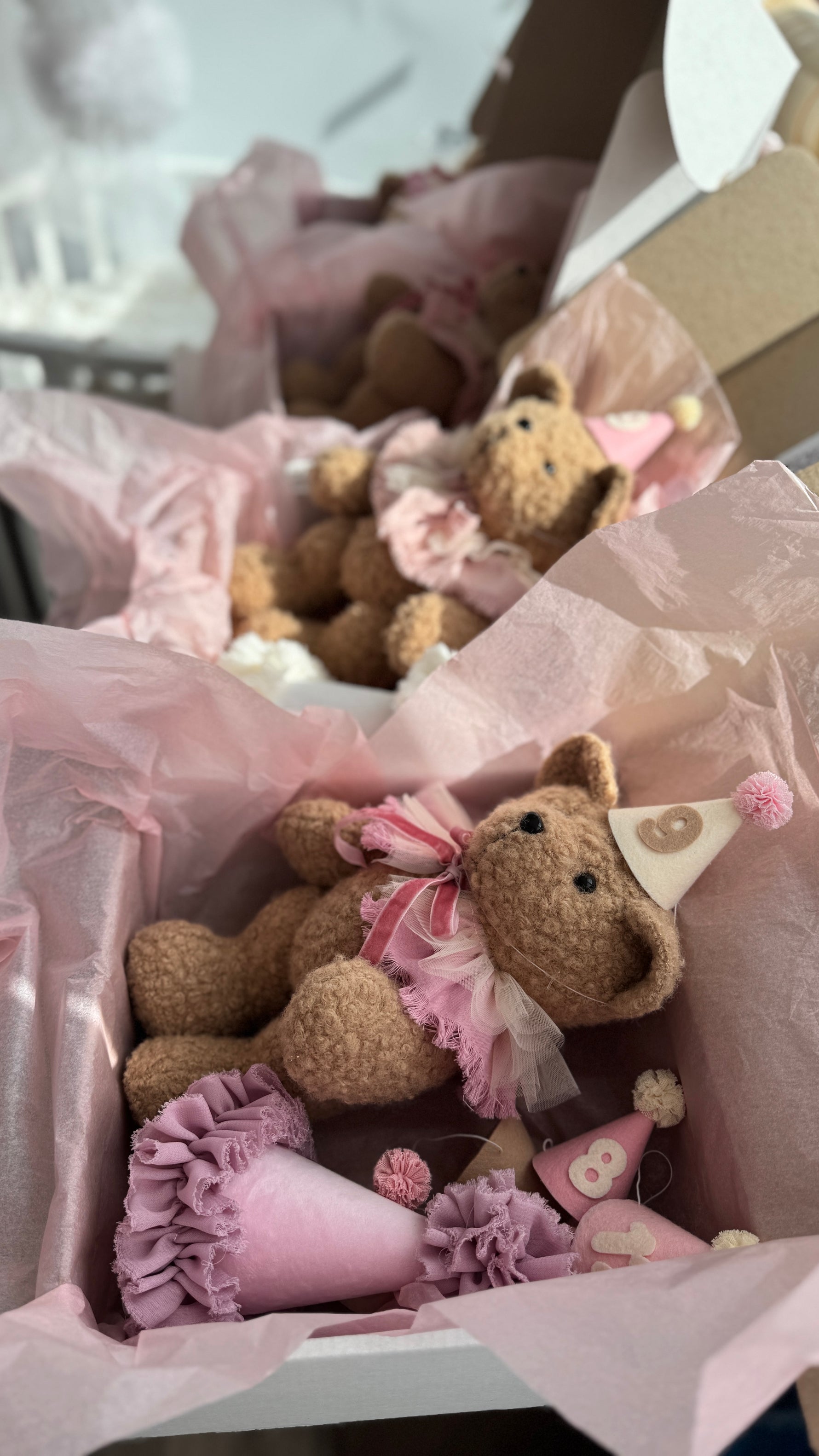 Scatole regalo aperte con orsetti di peluche e cappellini numerati rosa per la crescita del neonato