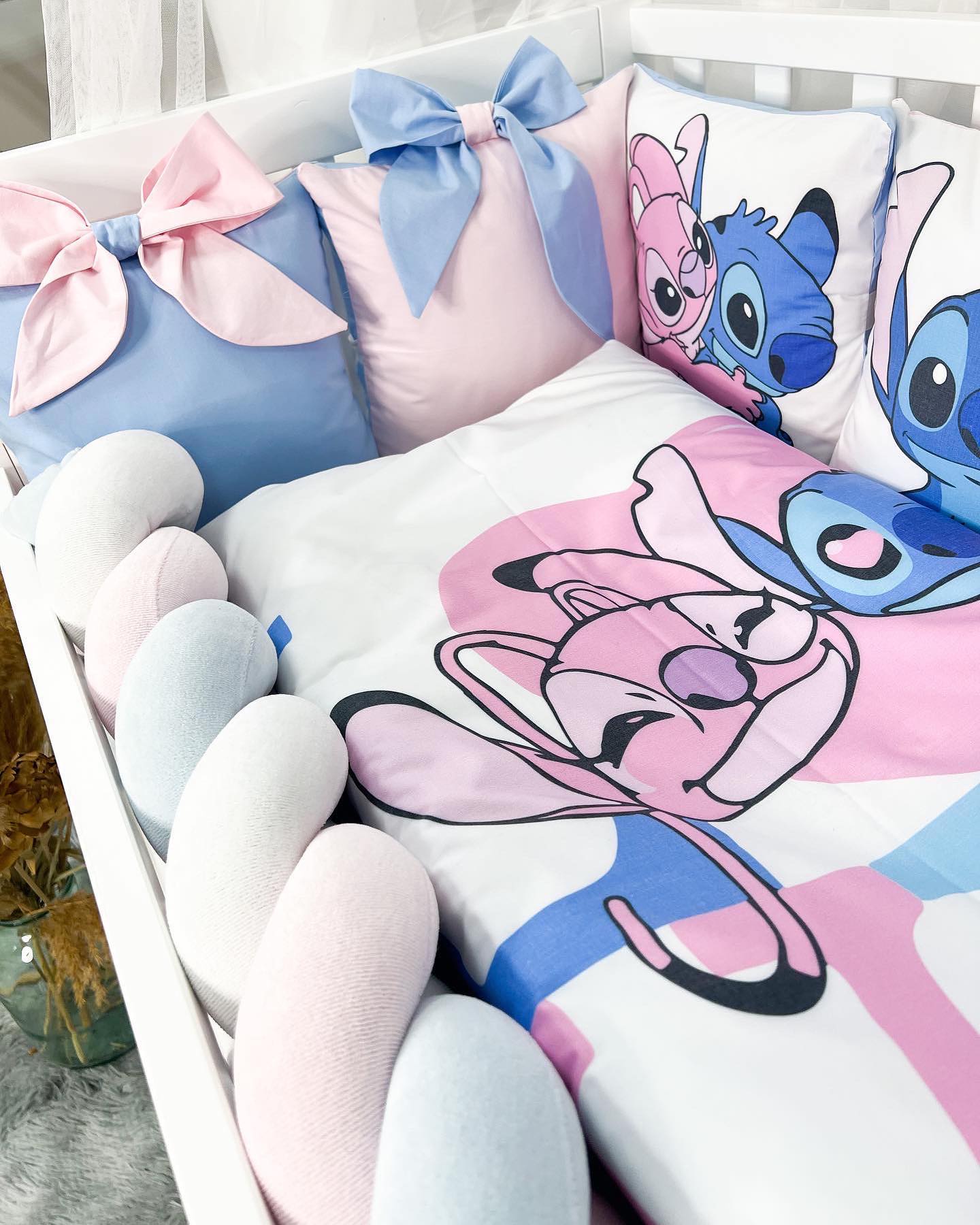 Dettaglio cuscini paracolpi sfoderabili rosa e azzurri con grandi fiocchi e treccia protettiva letto neonato