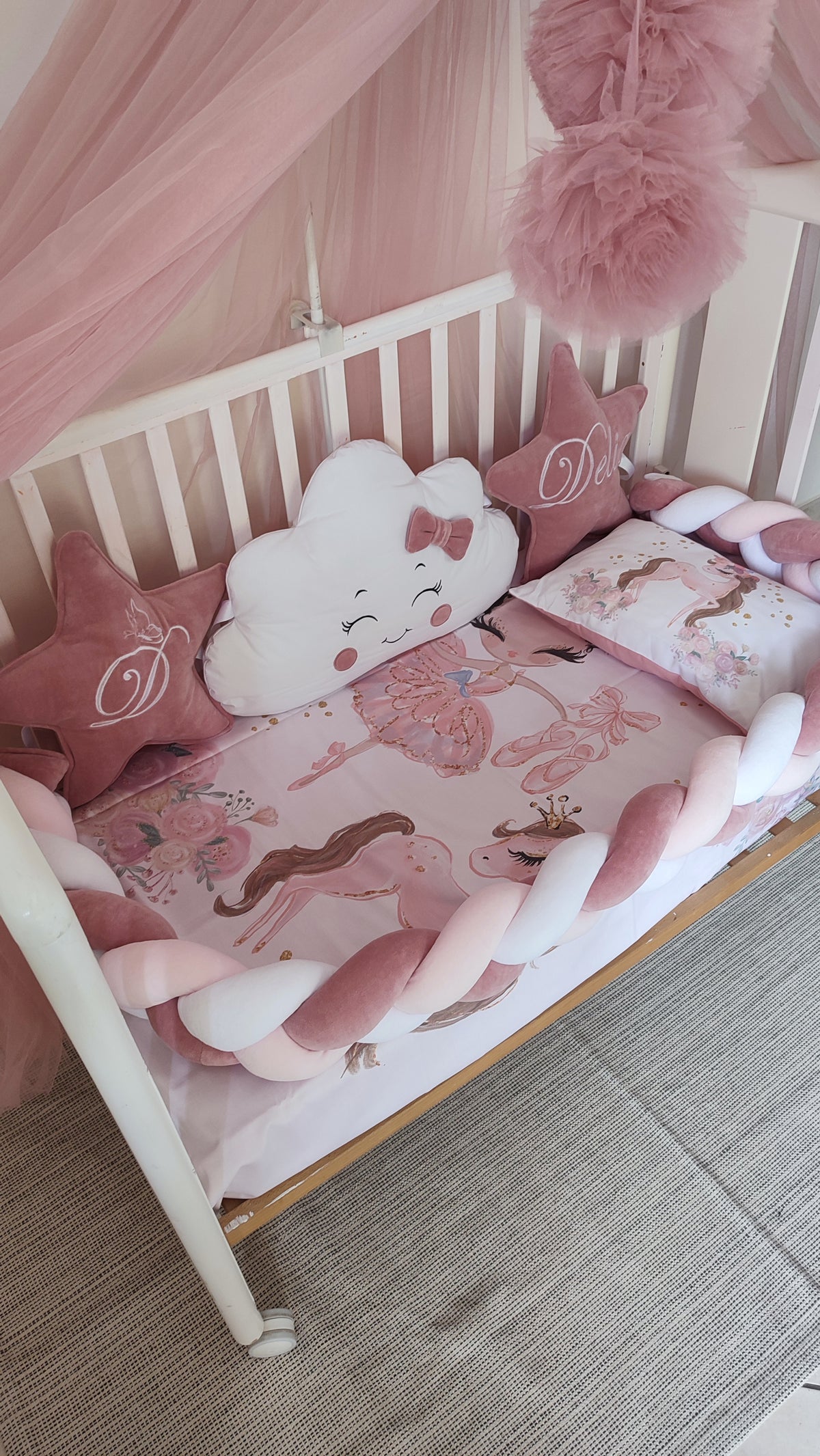 Dettaglio lettino neonata con cuscini stella velluto rosa antico con iniziale ricamata, nuvola bianca con fiocco e lenzuola stampate ballerina