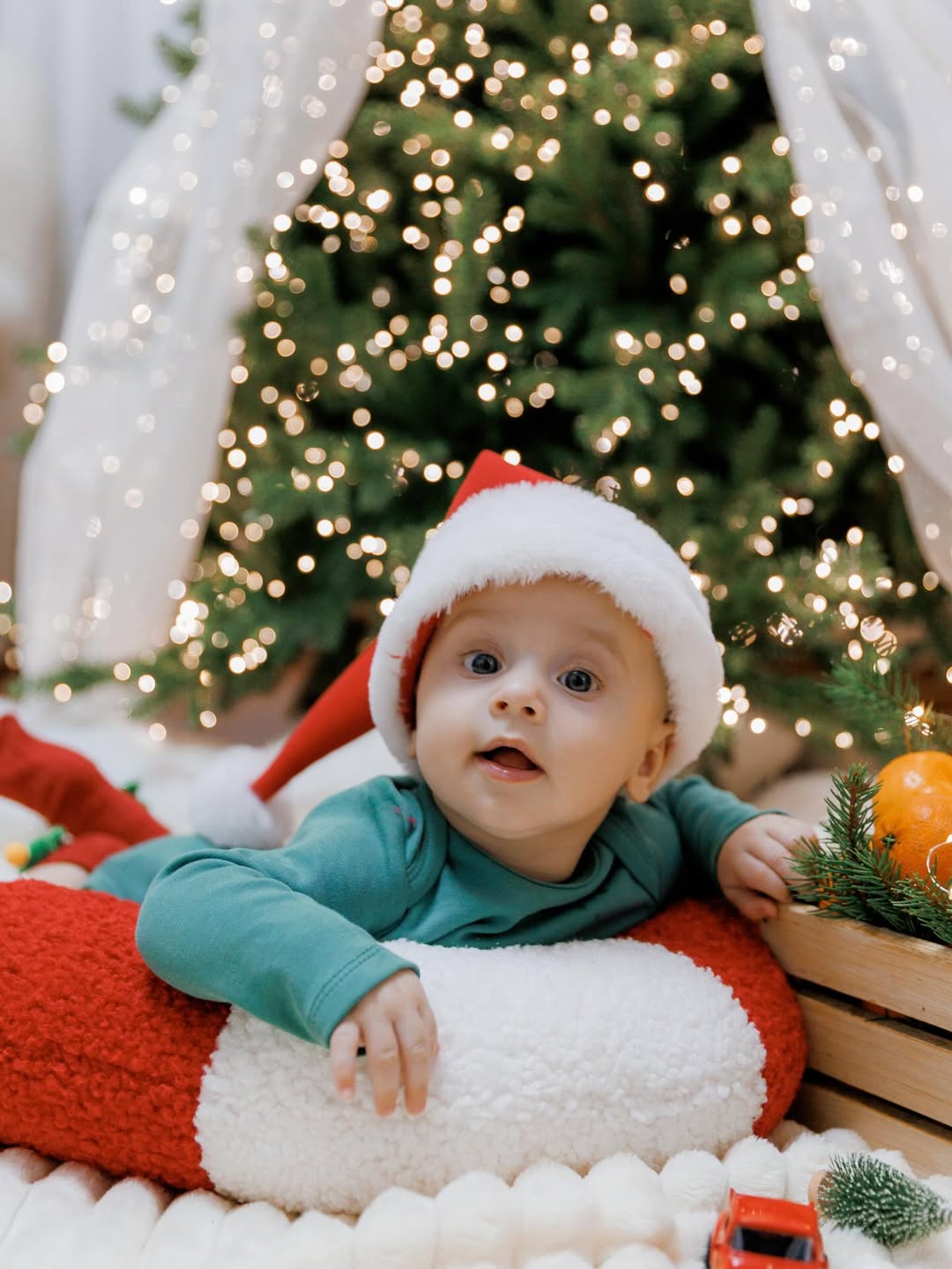 Neonato appoggiato a un cuscino bastoncino di zucchero in tessuto bouclé bianco e rosso sotto l'albero di Natale.
