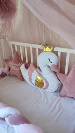 Cuscino cigno bianco con corona dorata e ali rosa per lettino neonata, affiancato da stelle velluto rosa con nome ricamato
