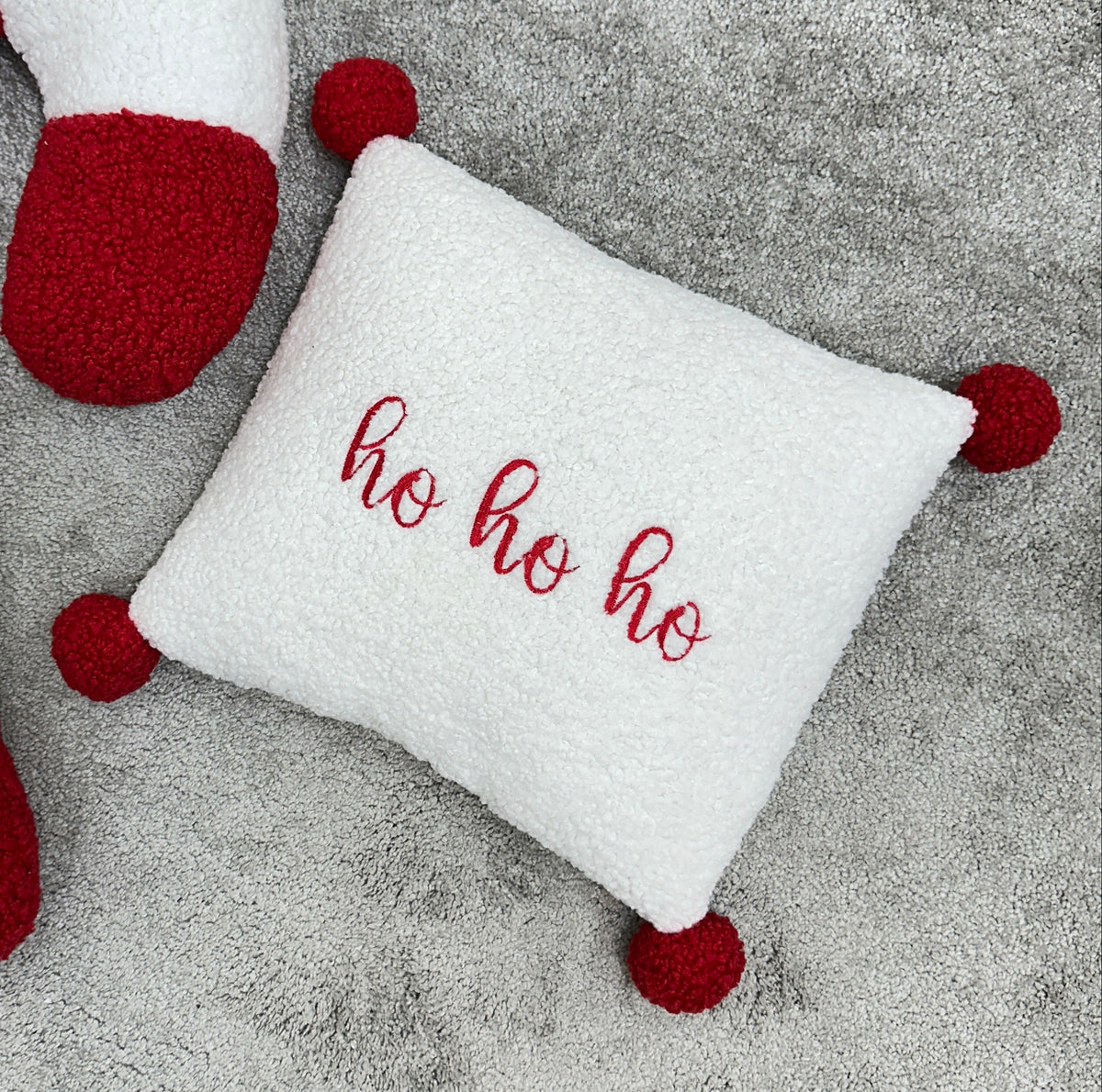 Dettaglio cuscino quadrato bianco ricamato ho ho ho con pon pon natalizi per letto e lettino
