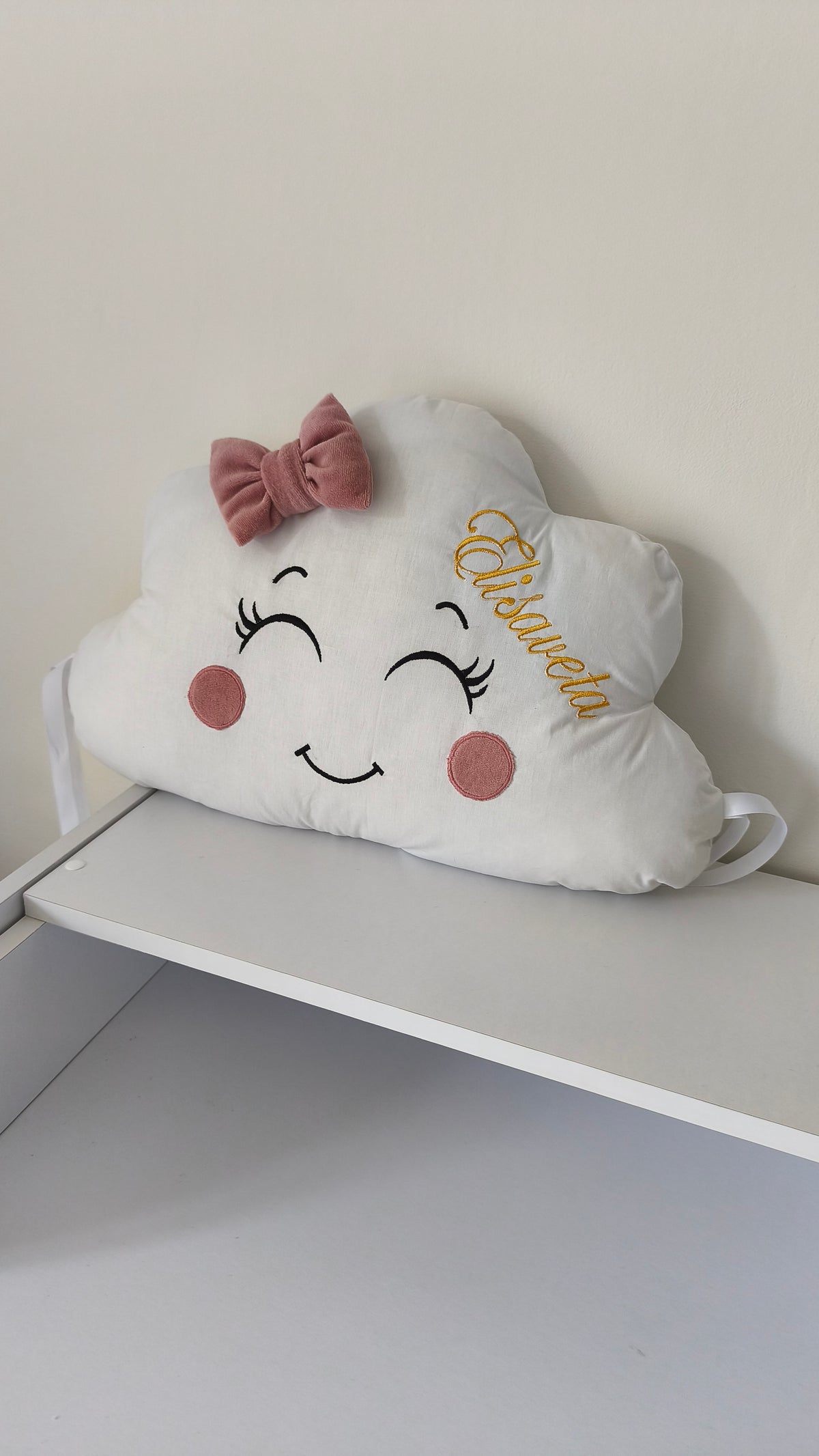 Cuscino nuvola paracolpi bianco con nome personalizzato ricamato in oro, fiocco rosa antico e nastri per lettino.