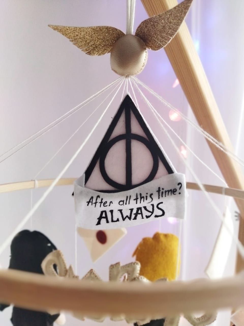 Dettaglio giostrina culla Harry Potter con boccino d'oro, simbolo doni della morte e scritta Always