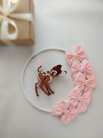 Dettaglio giostrina feltro con cerbiatto Bambi marrone, farfalla e grandi fiocchi rosa su sfondo bianco.
