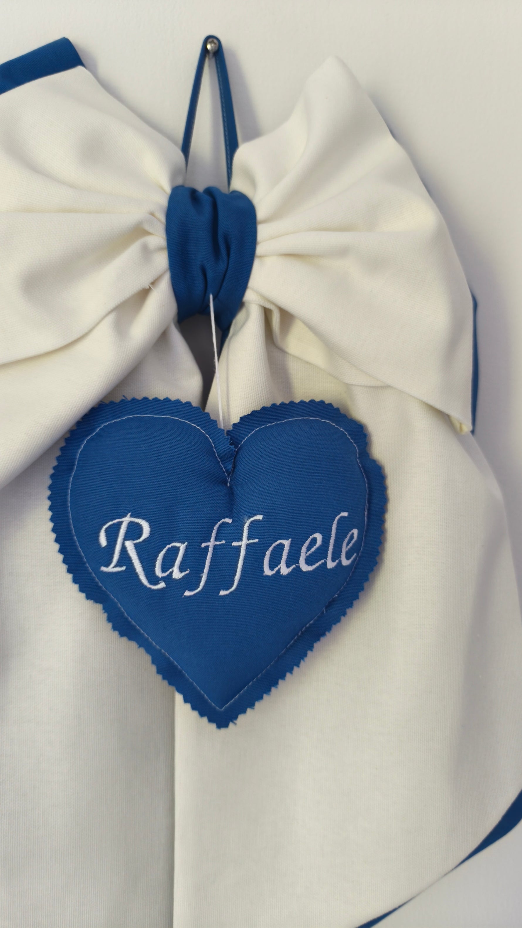 Dettaglio cuore blu ricamato con nome bambino su fiocco nascita panna