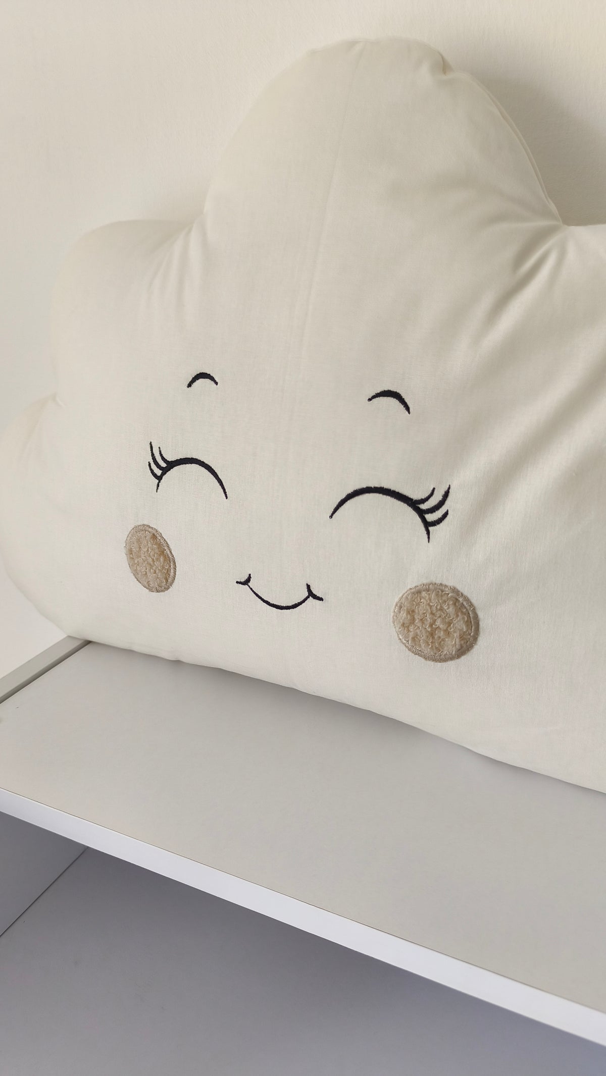 Dettaglio del ricamo di un cuscino a nuvoletta beige e panna, ideale come paracolpi e arredo culla per neonati.
