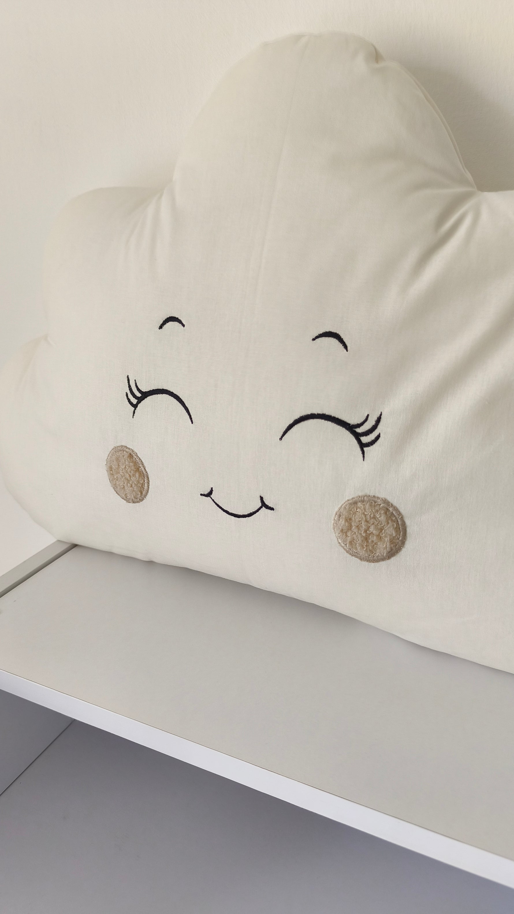 Dettaglio del ricamo di un cuscino a nuvoletta beige e panna, ideale come paracolpi e arredo culla per neonati.