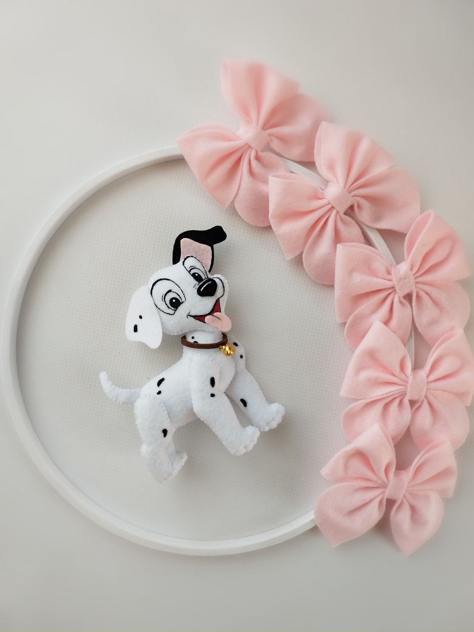 Dettaglio giostrina feltro con cucciolo dalmata bianco e nero e grandi fiocchi rosa su cerchio bianco.