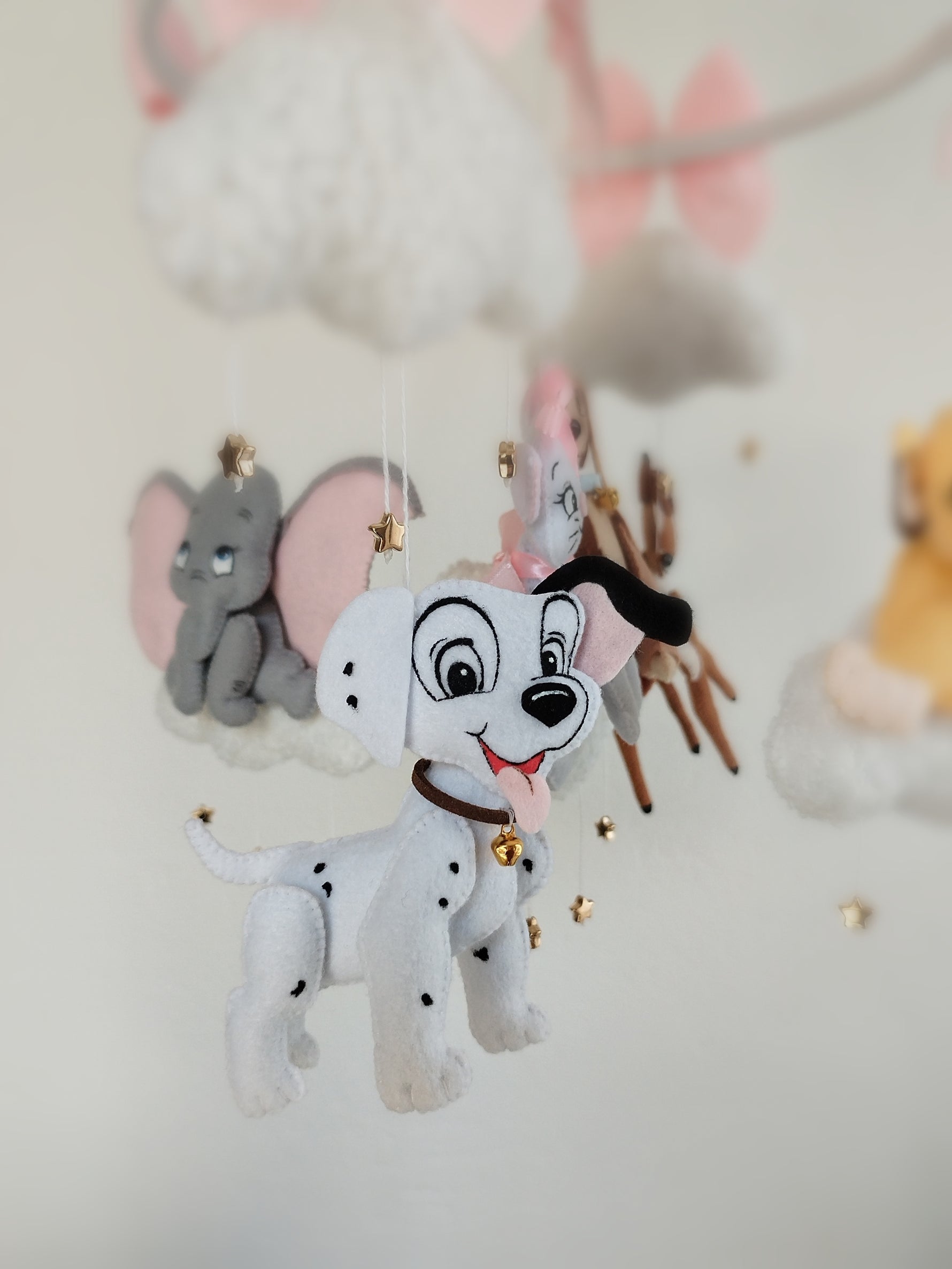 Dettaglio giostrina feltro con cucciolo dalmata bianco e nero e Dumbo grigio appesi a nuvole soffici.