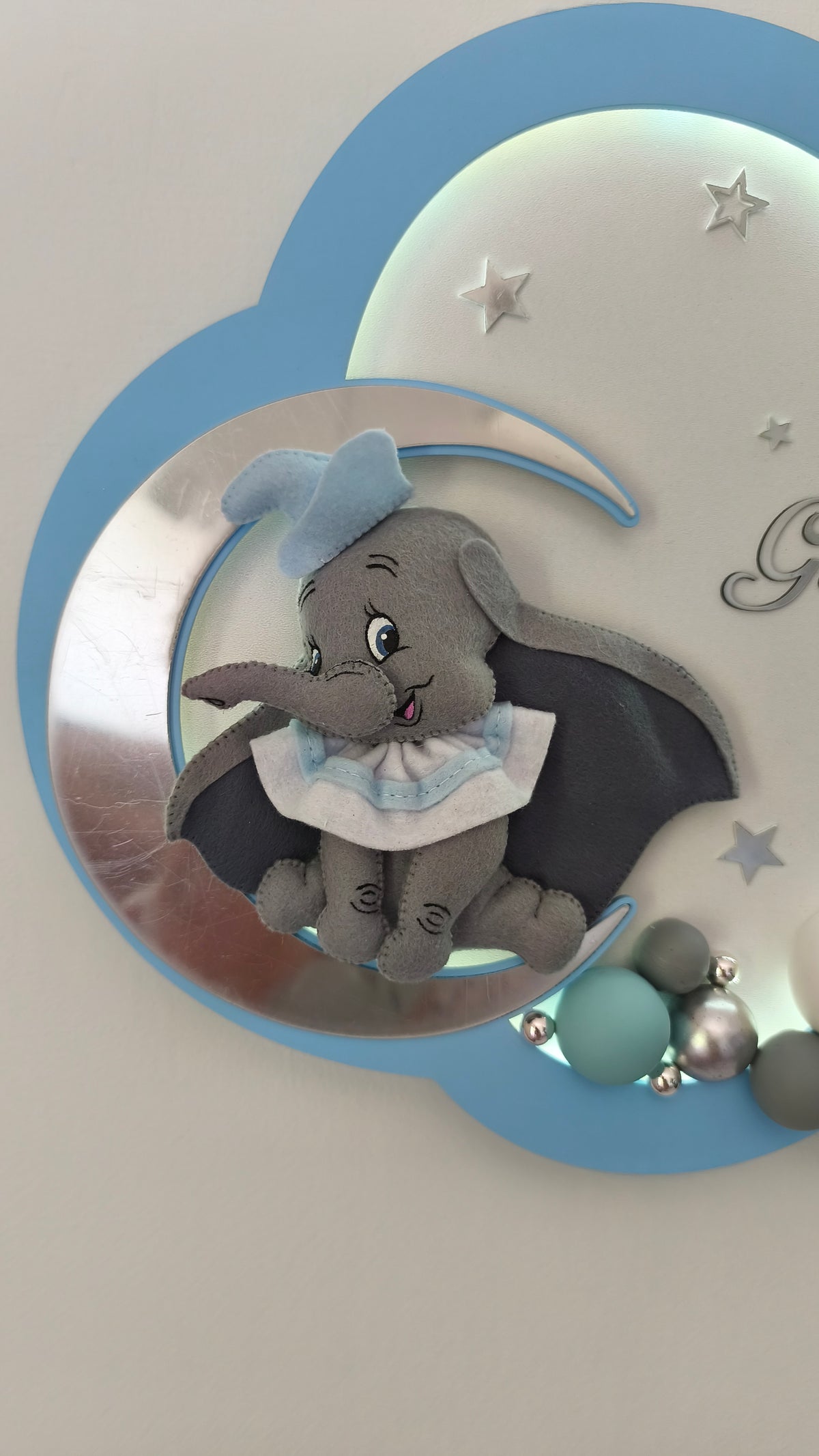 Dettaglio elefantino Dumbo in feltro su luna specchiata e sfere tiffany e grigie. Luce notturna personalizzata bimbo