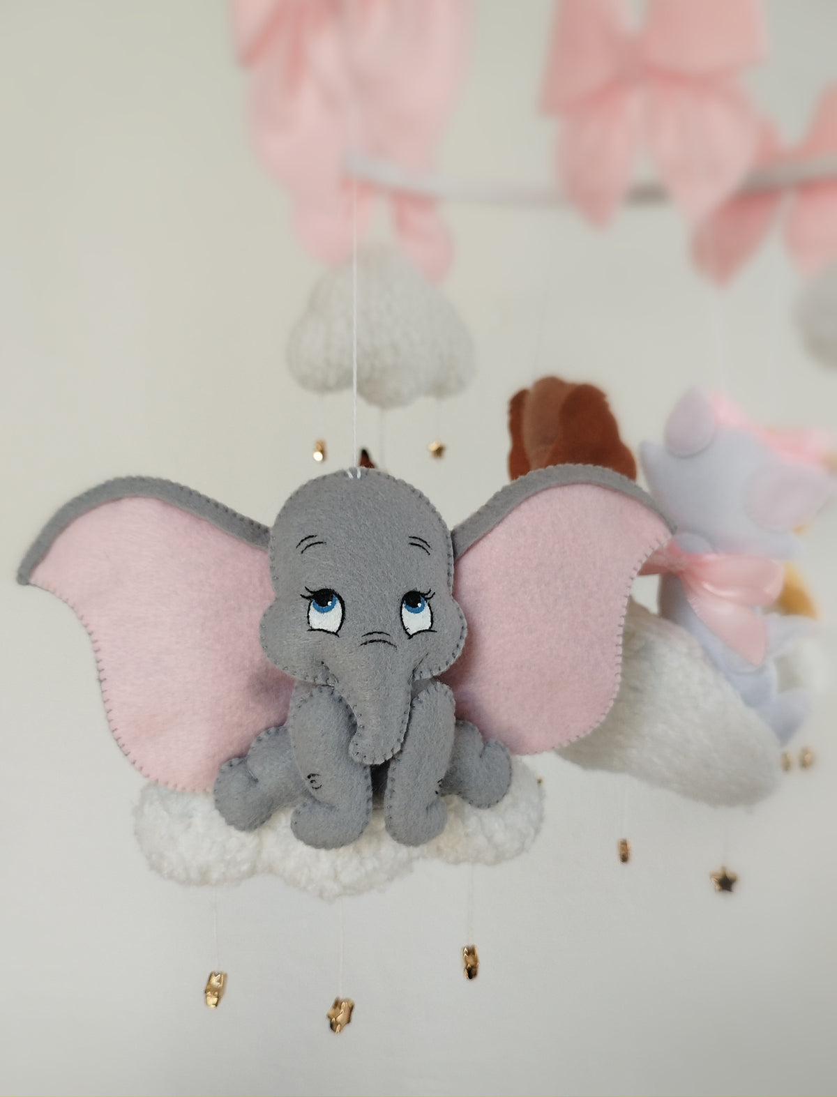 Dettaglio giostrina feltro con elefantino Dumbo grigio su nuvola bianca, grandi orecchie rosa e stelline