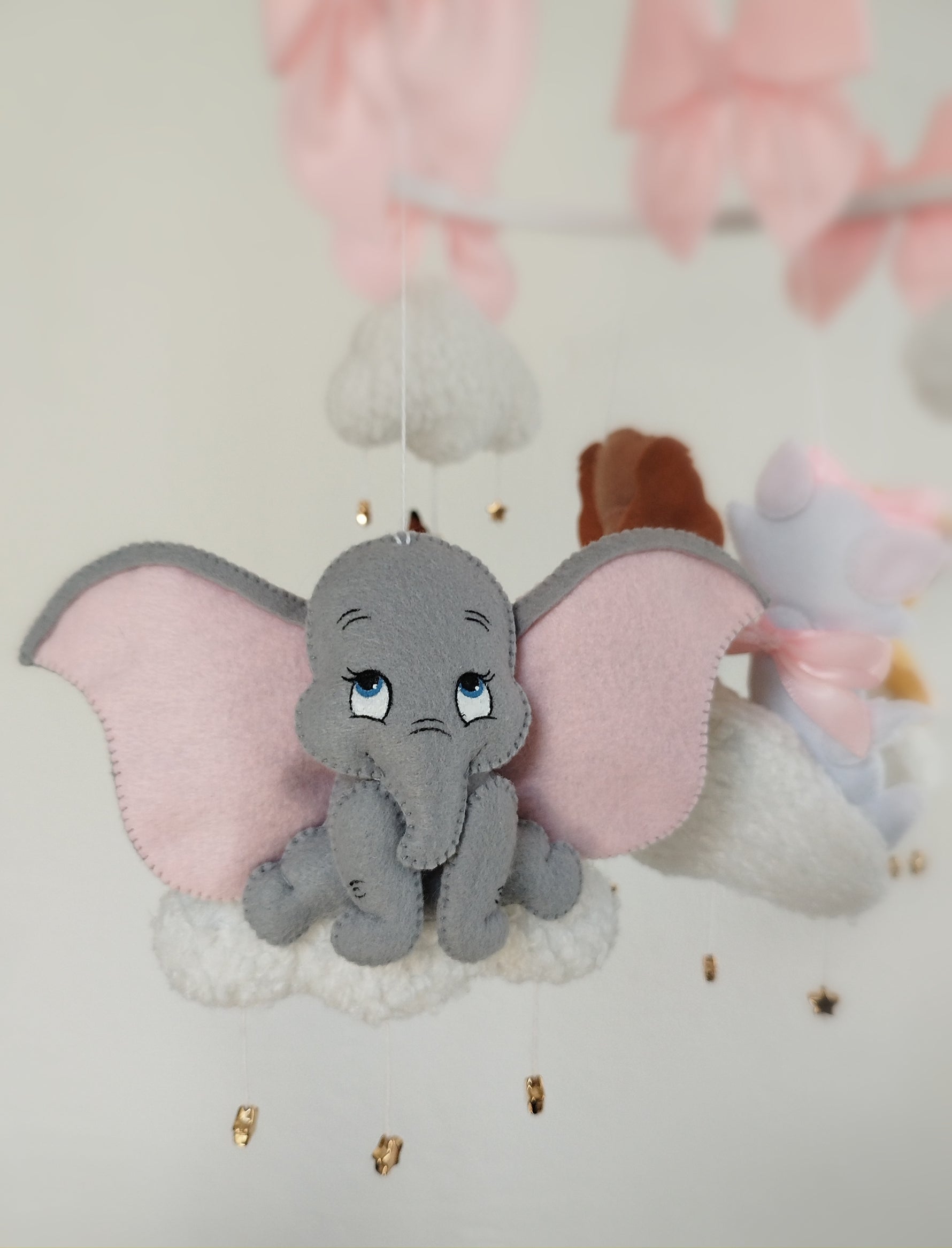 Dettaglio giostrina feltro con elefantino Dumbo grigio su nuvola bianca, grandi orecchie rosa e stelline