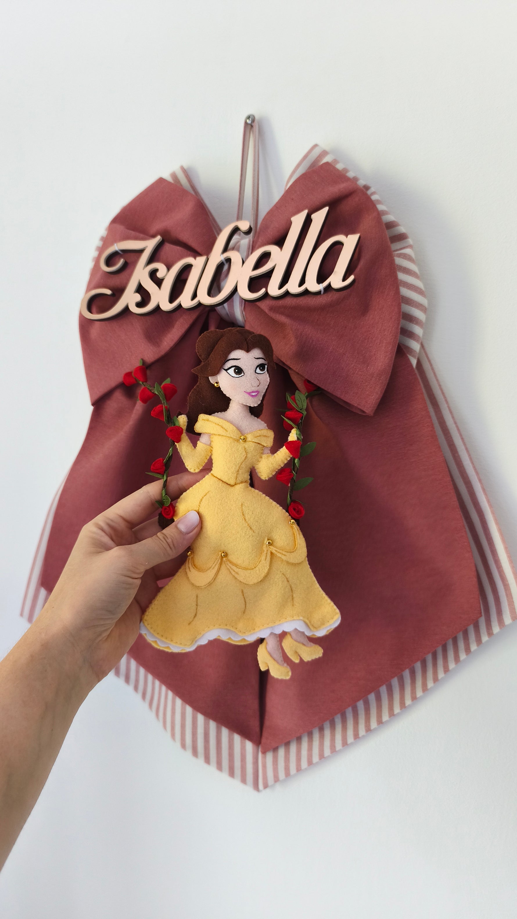 Dettaglio fiocco nascita rosa antico con nome bambina e principessa in abito giallo su altalena di rose
