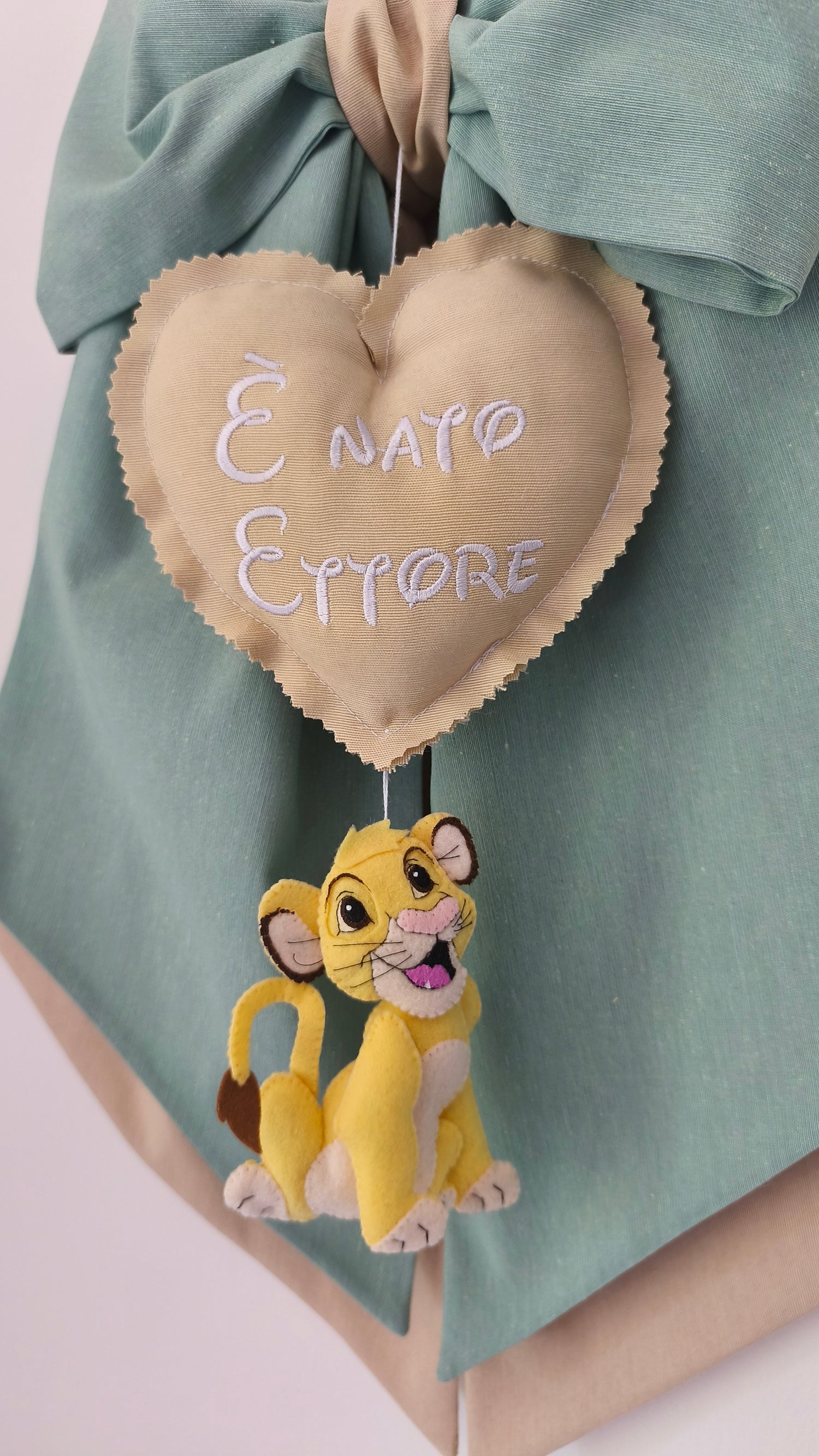 Dettaglio fiocco nascita verde salvia con cuore beige ricamato personalizzabile e piccolo Simba Disney in feltro